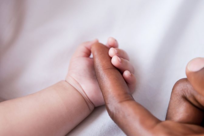 Close-up of little baby holding fathers finger